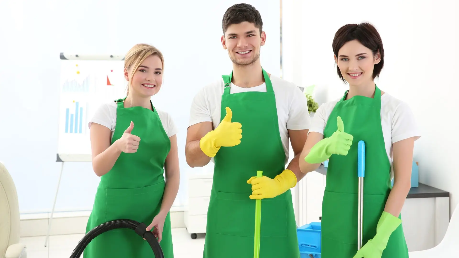 Three people in green aprons smiling and giving a thumbs-up gesture.